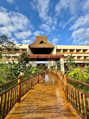 A wooden pathway leading to a building with a thatched roof and multiple balconies. - Hotel Mundo Maya Edzná (Tixmucuy)