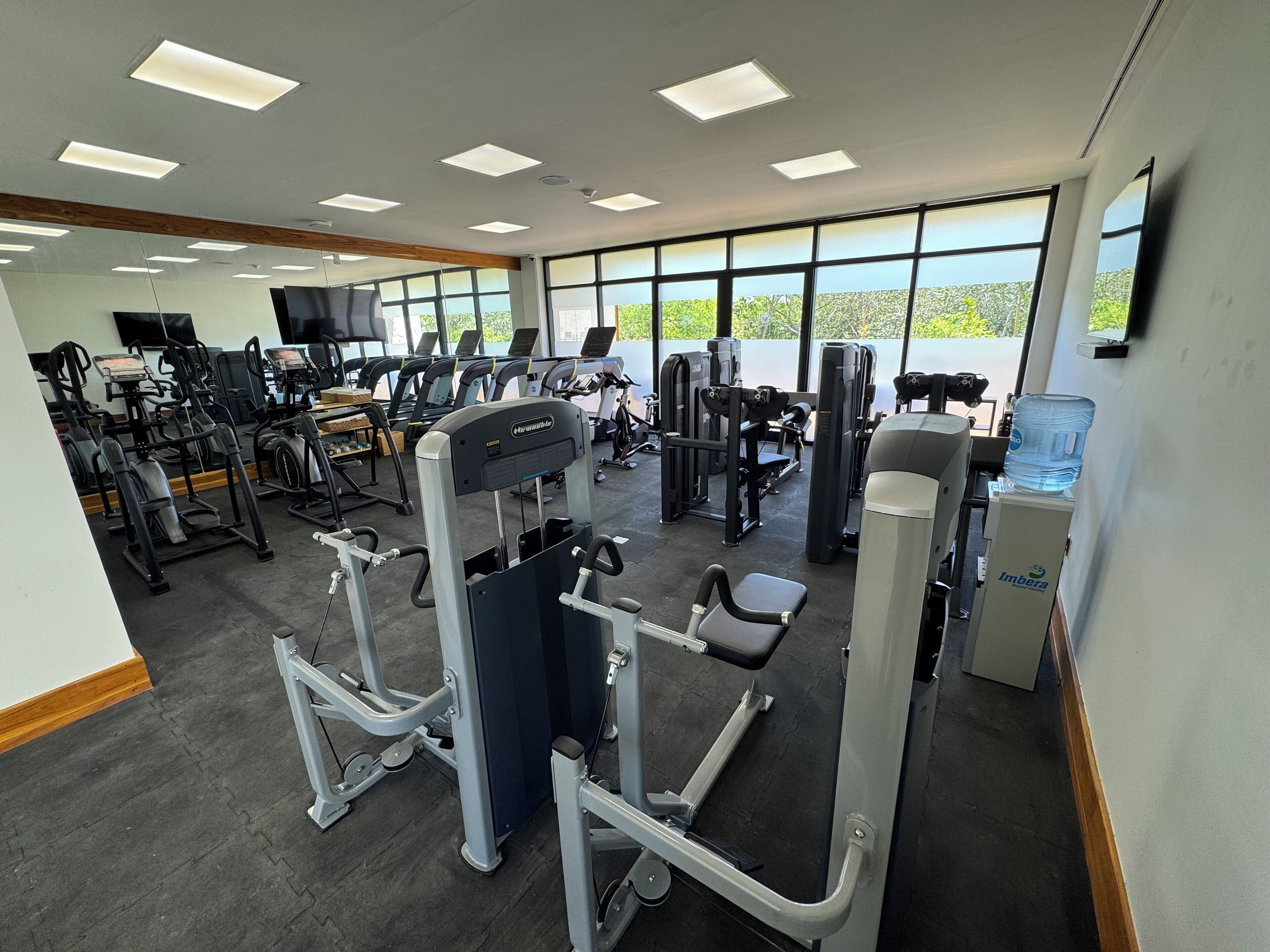 A gym with various exercise machines, large windows, and a water dispenser.