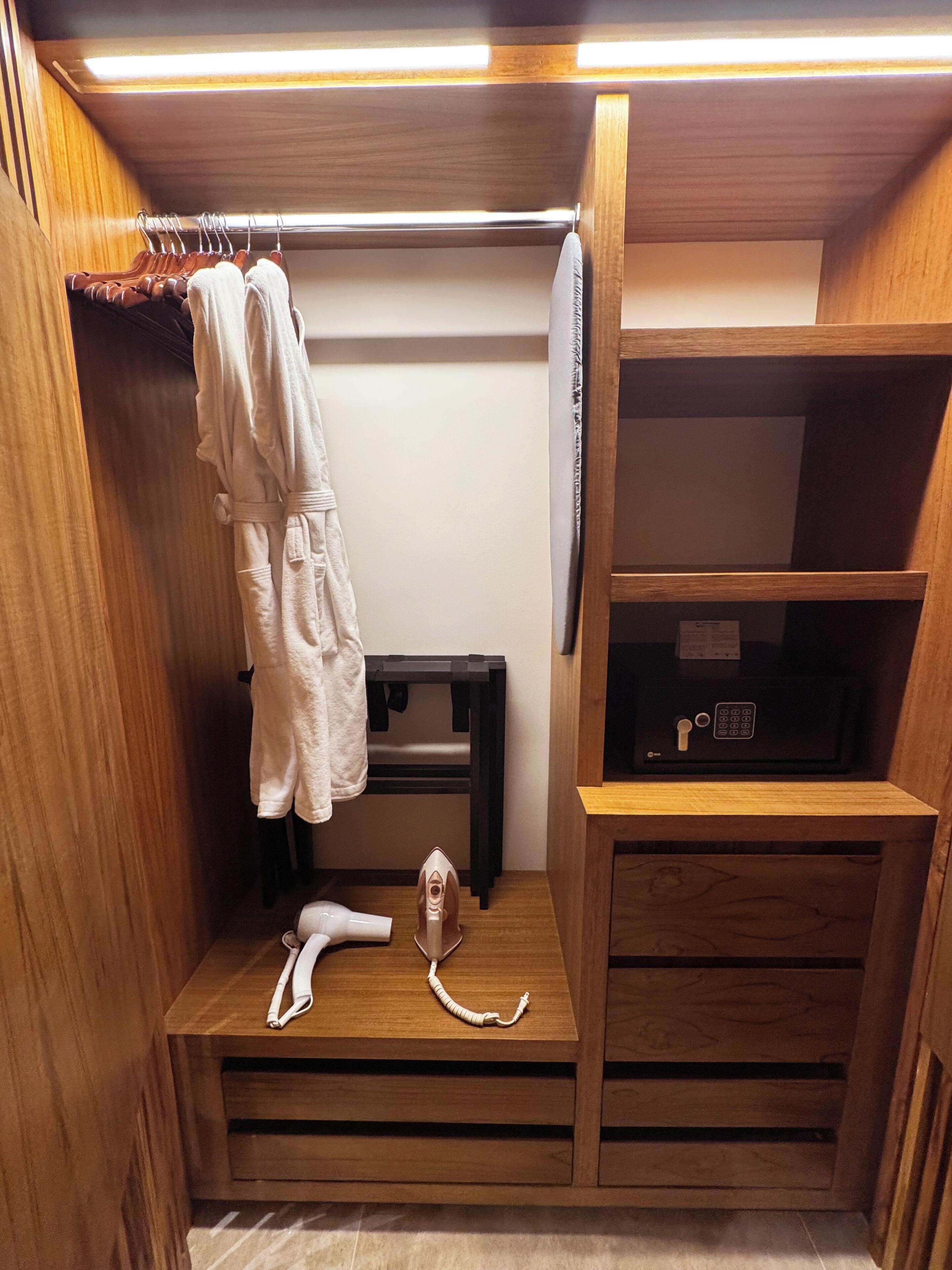 Un armario de madera con estantes, una barra para colgar ropa y una plancha pequeña.