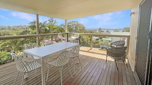 A covered outdoor area with a wooden deck, white metal chairs, a table, and a grill. - Spacious 4-Bed Coastal Home with Water Views (Batehaven)