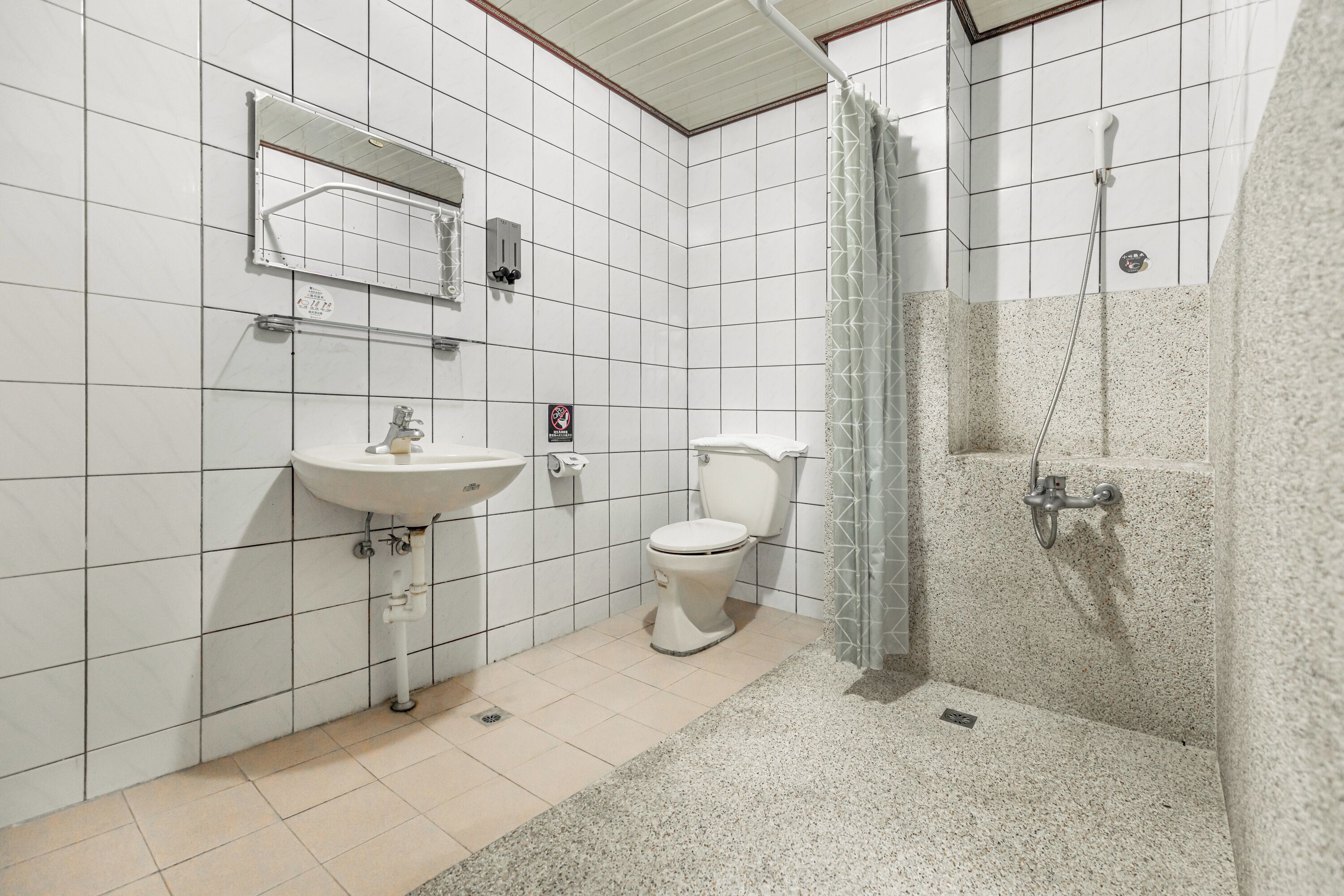A bathroom with white tiled walls, a white sink, a toilet, and a shower area with a glass door.