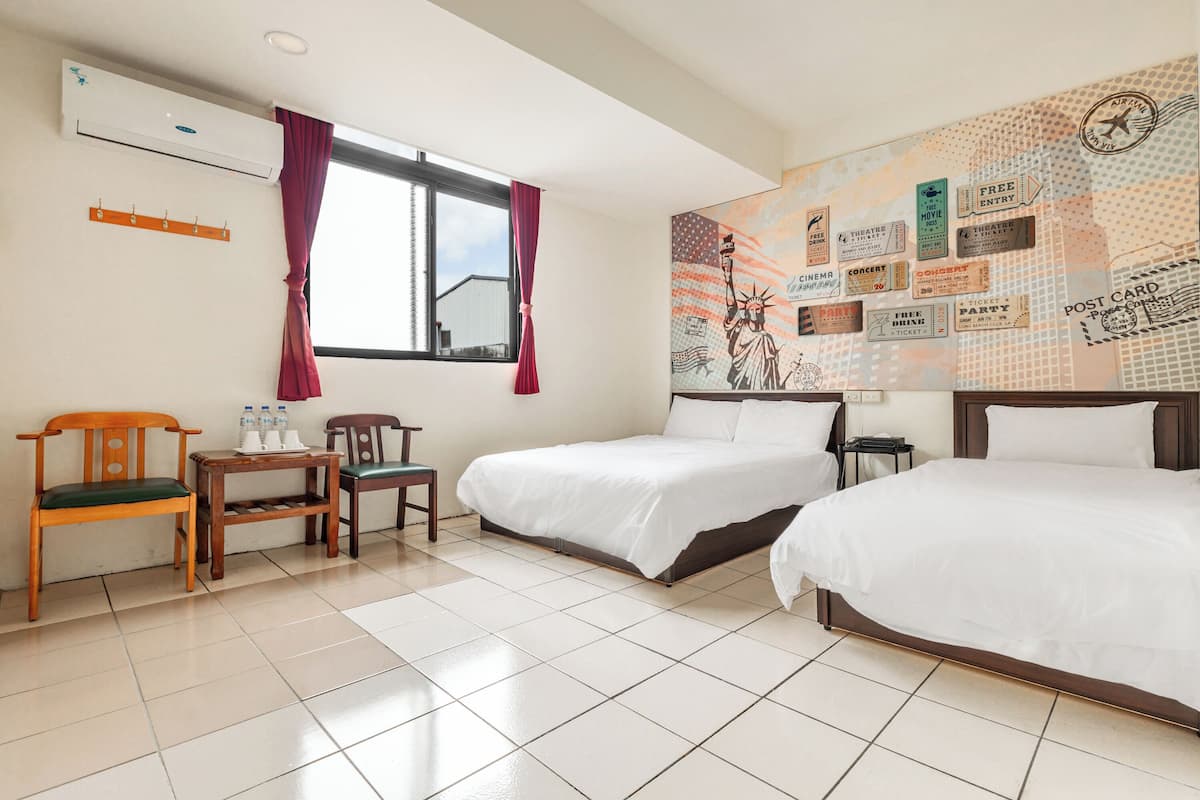 Ein Hotelzimmer mit zwei Betten, einem Schreibtisch, einem Stuhl, einer Klimaanlage und einer Wand mit verschiedenen Postern.