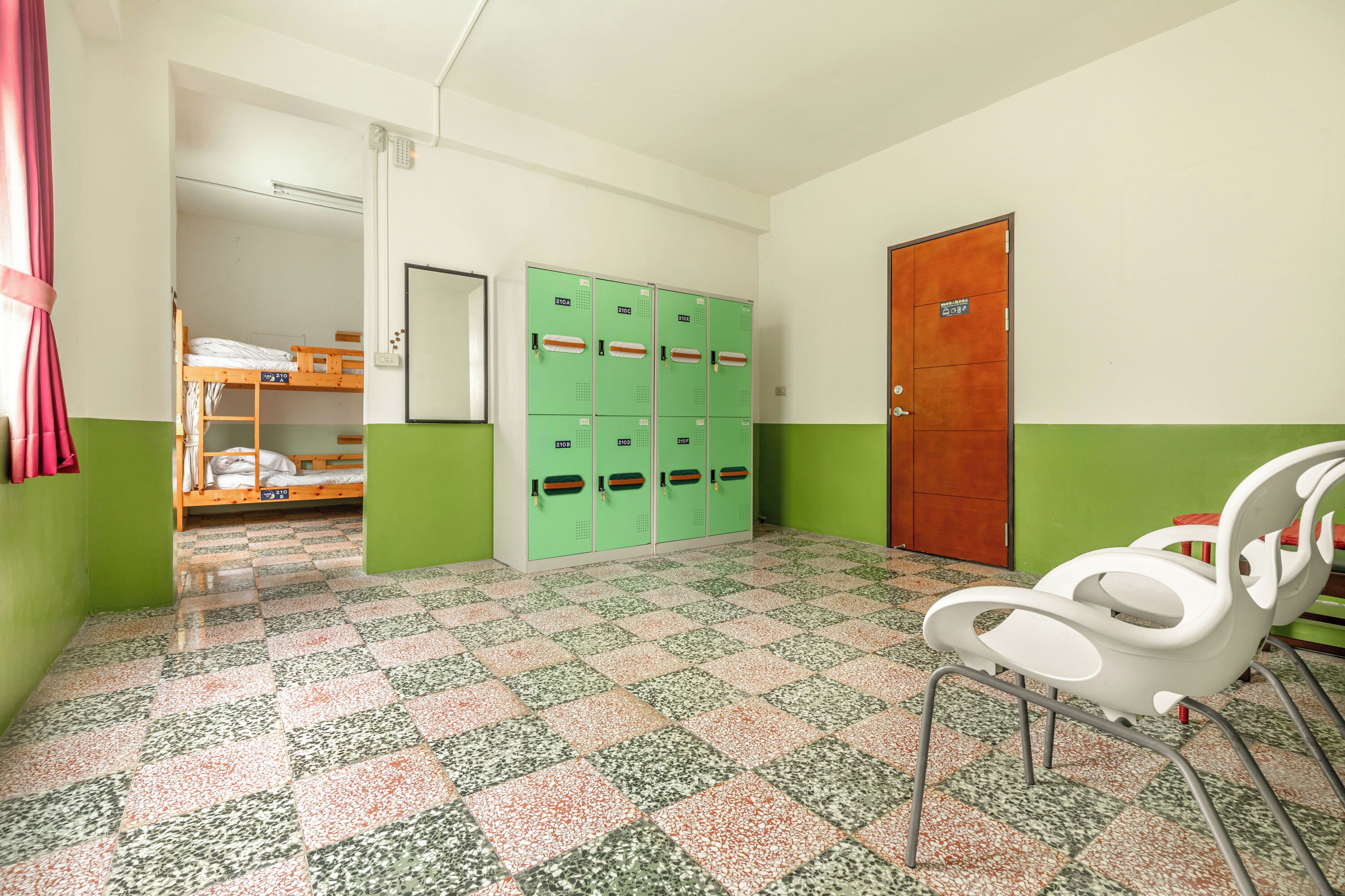 A room with bunk beds, green lockers, a white chair, and a wooden door.