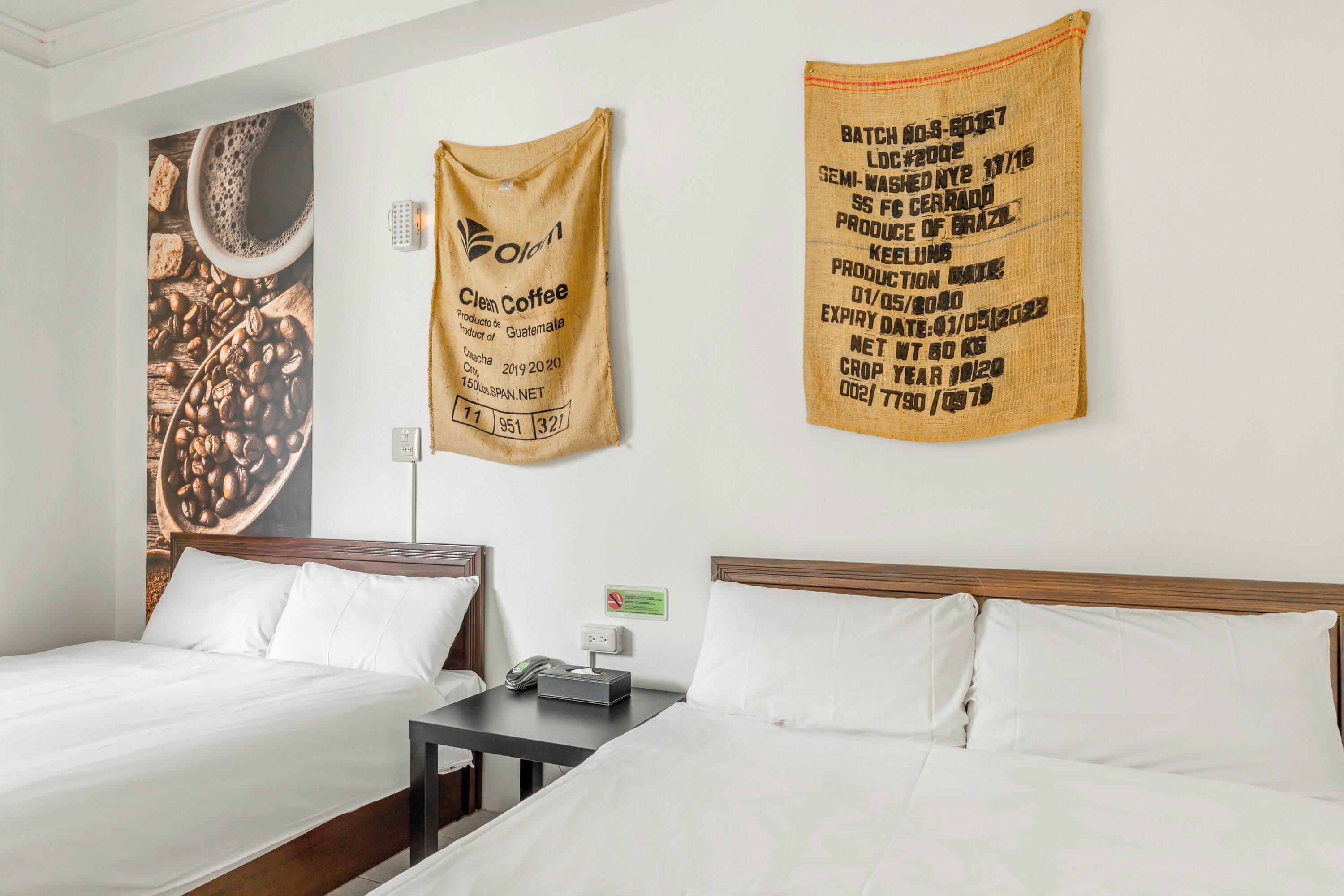 A hotel room with two beds, a nightstand, and a wall with coffee-themed decorations.