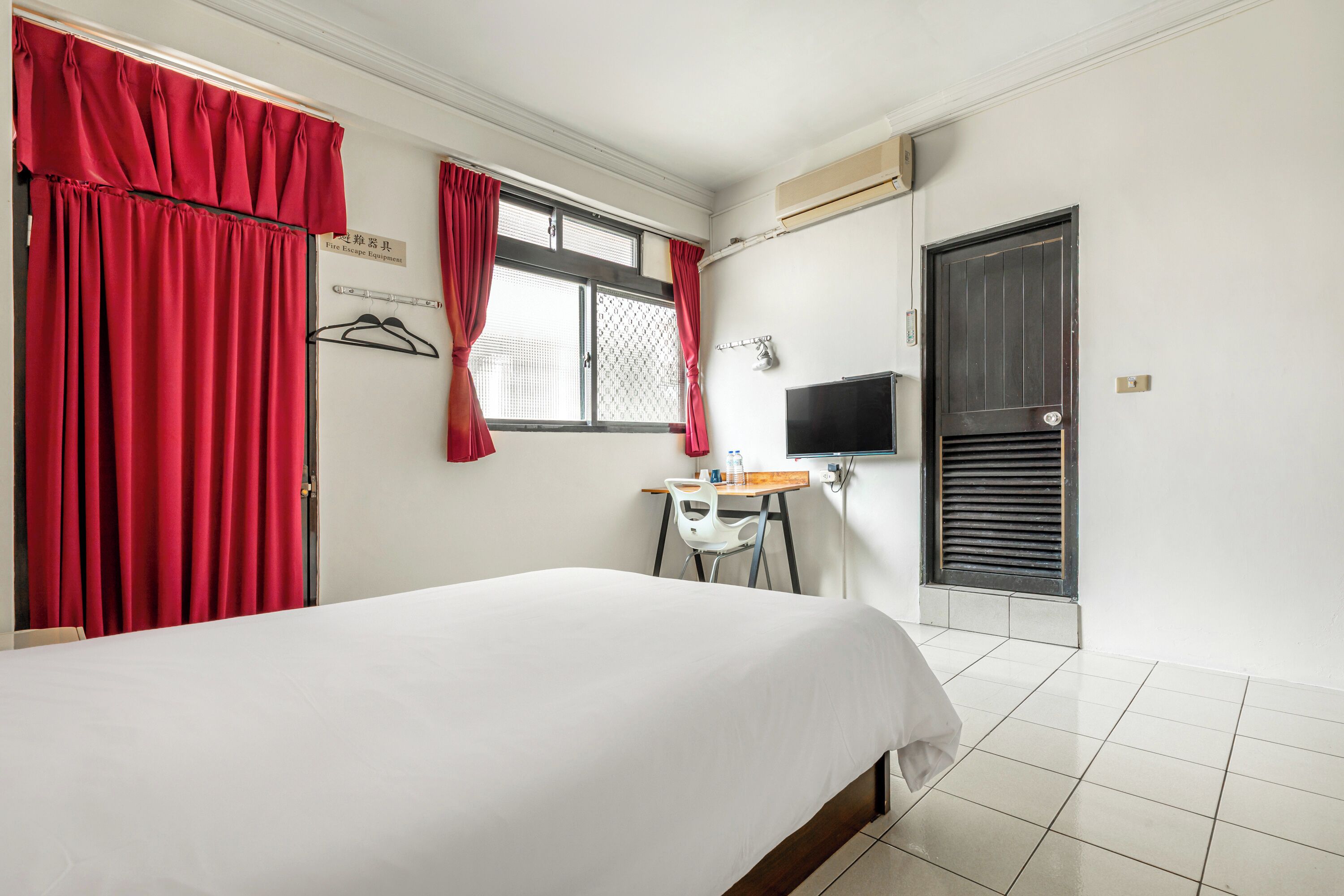 Une chambre d’hôtel avec un lit, un bureau, une chaise, une télévision et une porte.