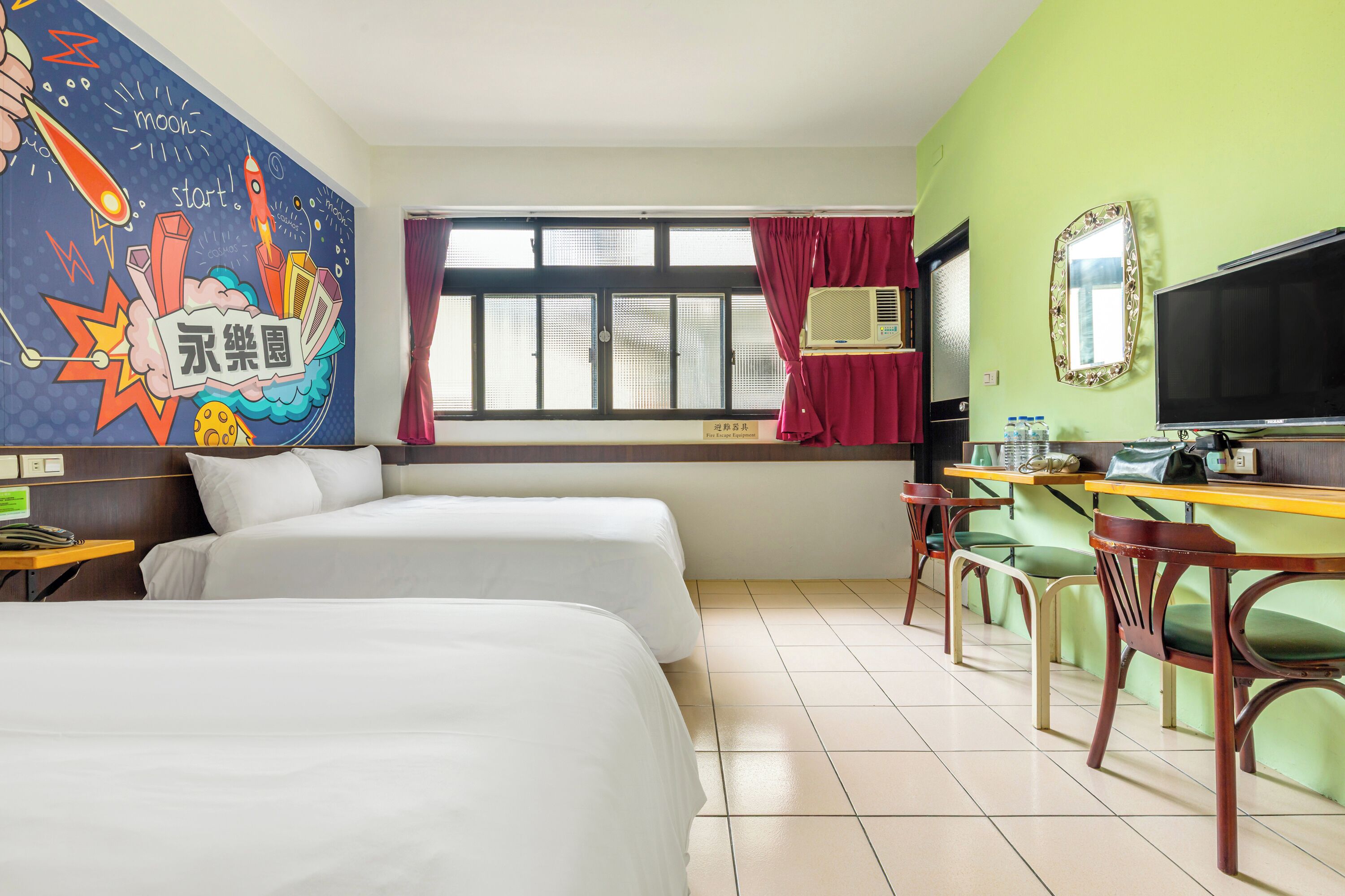 Una habitación de hotel con dos camas, un escritorio con una silla, un televisor y una ventana con cortinas.