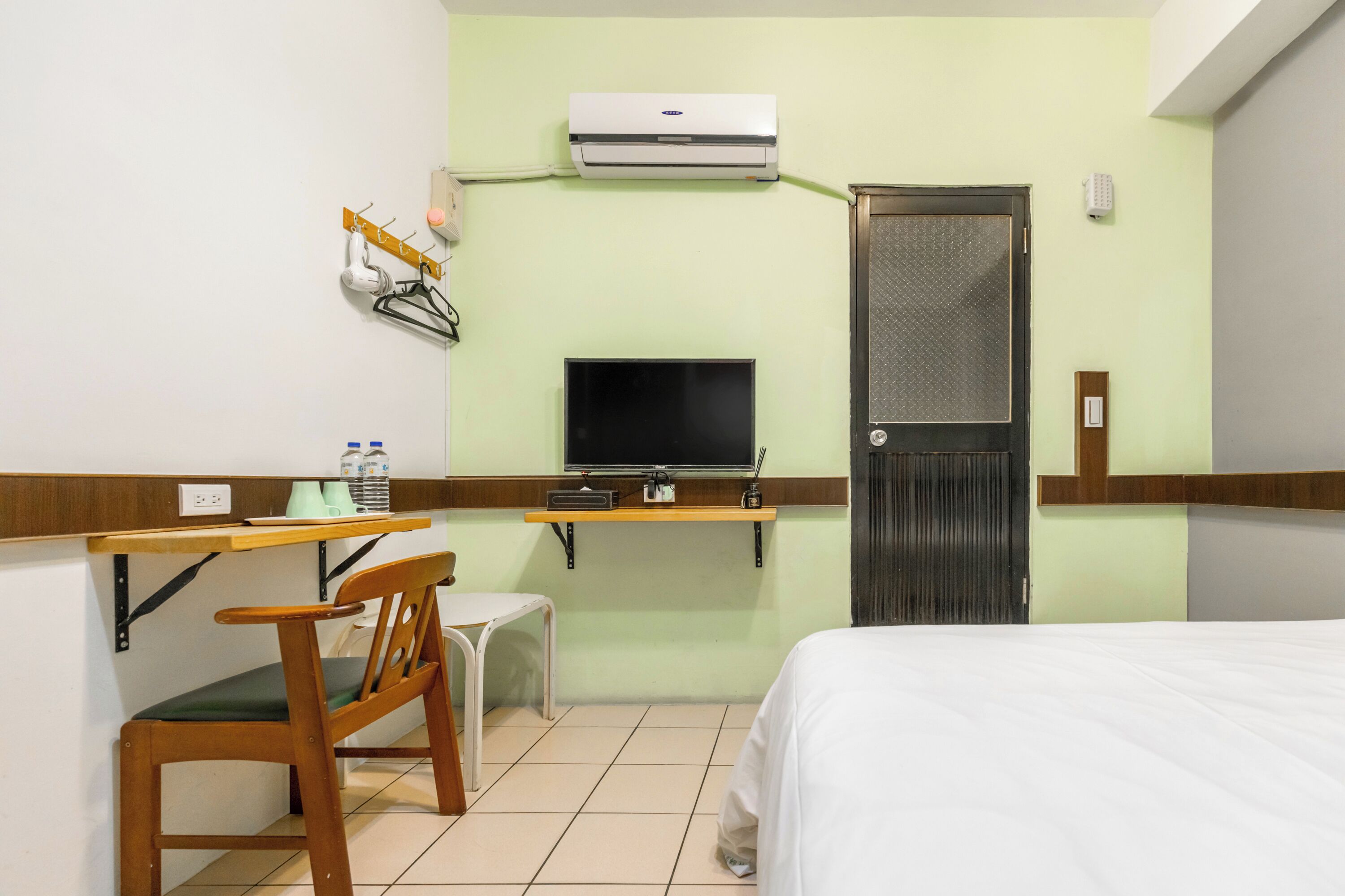 Quarto de hotel com cama, escrivaninha e cadeira, televisão, ar condicionado e porta.