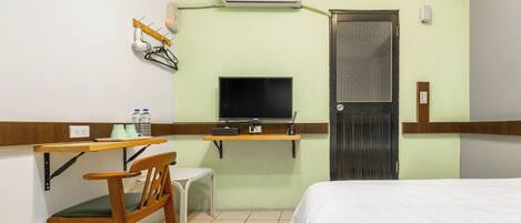 Quarto de hotel com cama, escrivaninha e cadeira, televisão, ar condicionado e porta.