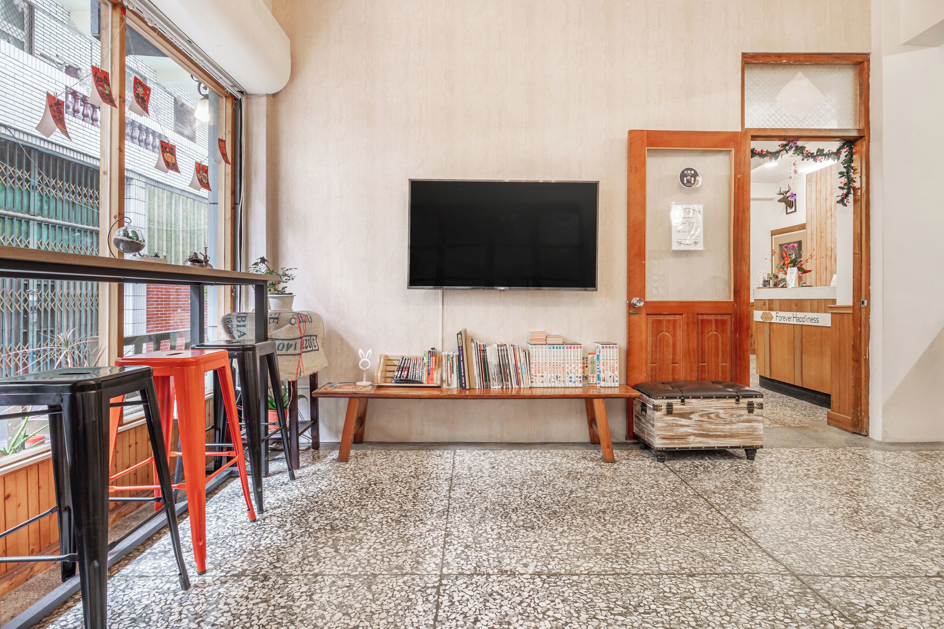 A room with a large window, a flat-screen TV, a wooden bench, and a small table with books.