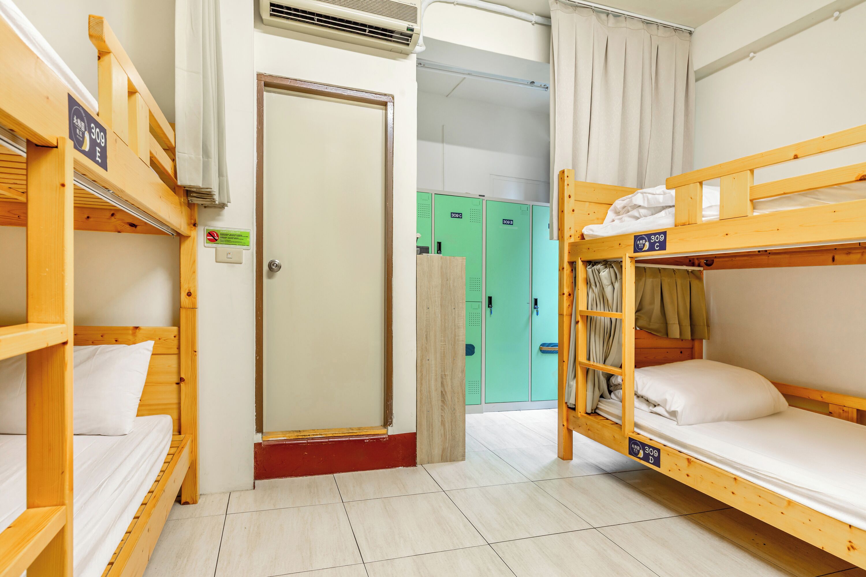 A dormitory room with bunk beds, a door, and green lockers in the background.