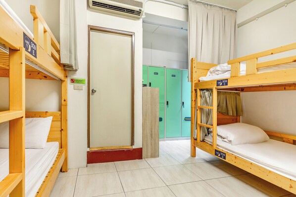 Une chambre de dortoir avec des lits superposés, une porte et, au fond, des casiers verts.