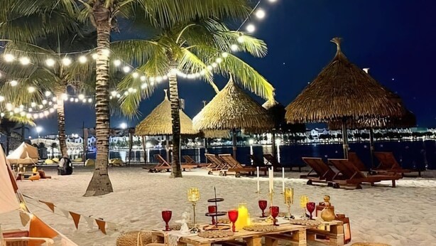 A beachside dining setup with thatched umbrellas, string lights, and beach chairs. - The Zenpark Tower - Vinhomes Ocean Park (Hanoi)
