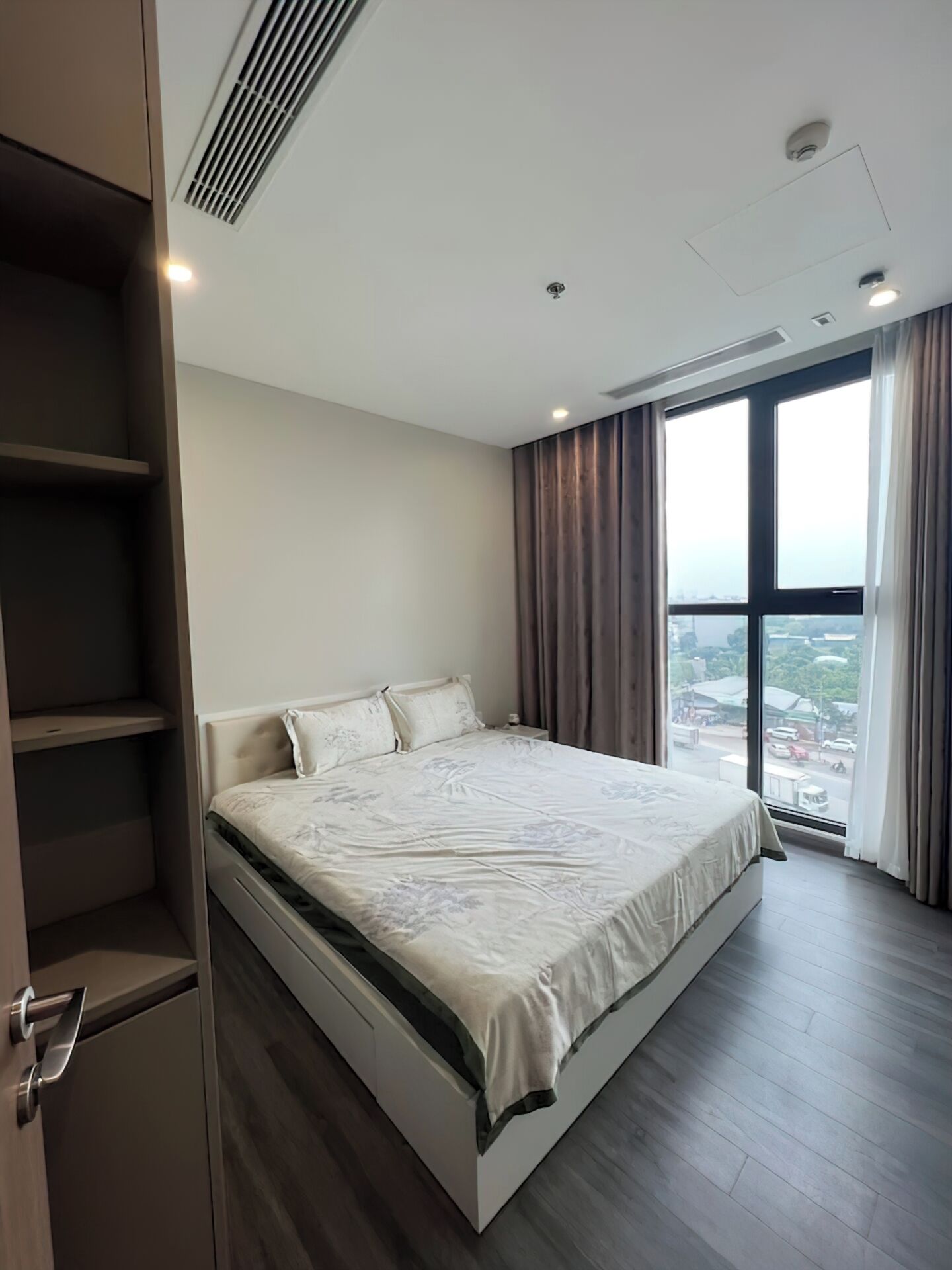 A modern bedroom with a large bed, built-in wardrobe, and a city view through the window.