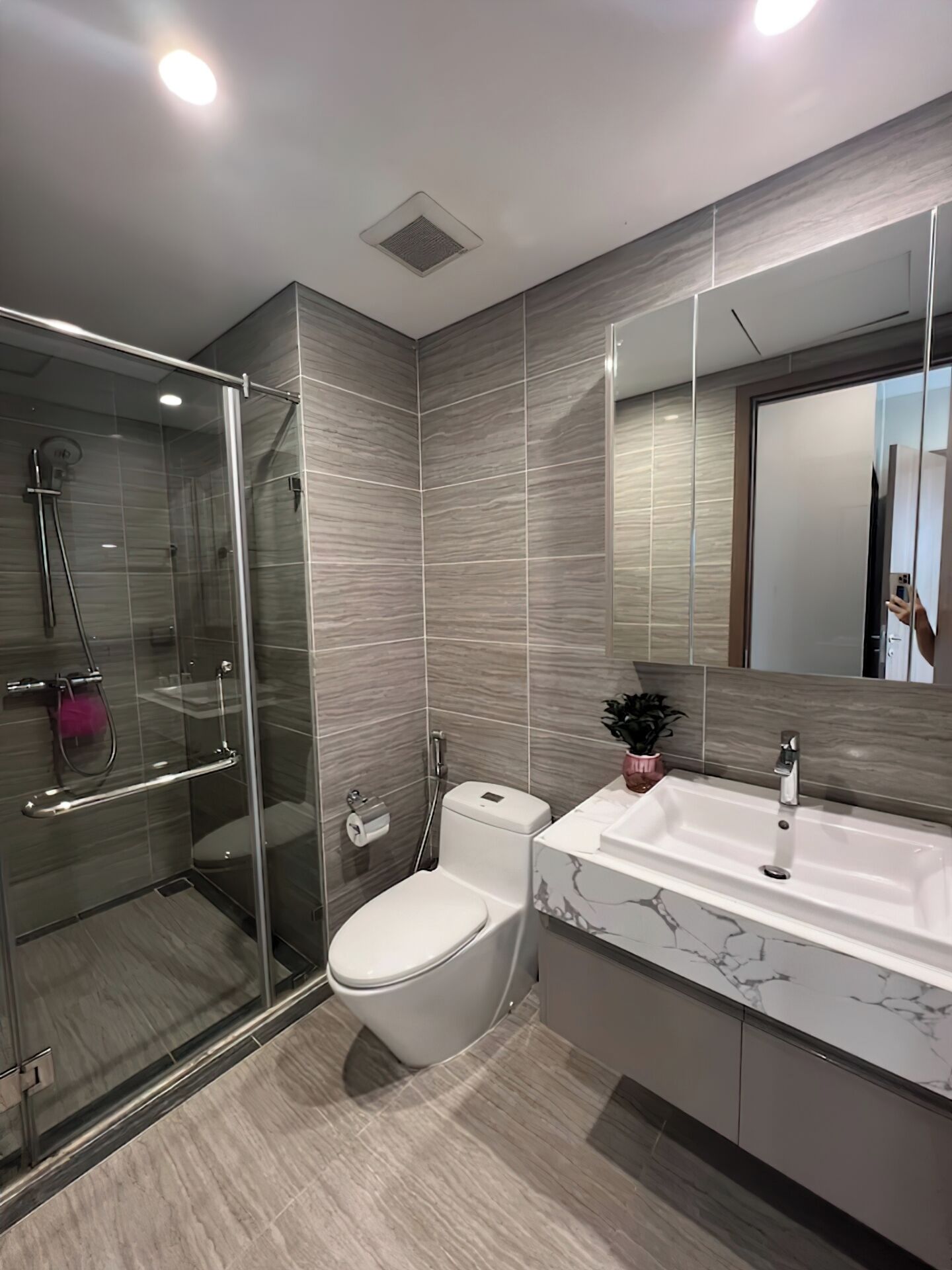 Ein modernes Badezimmer mit einer Glaskabine, einer weißen Toilette und einem мраморплотном Waschbecken.