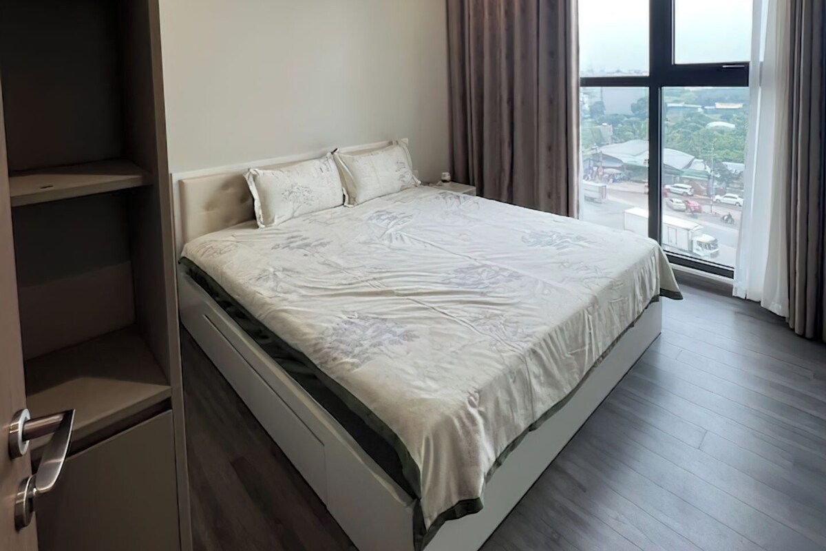 A modern bedroom with a large bed, built-in wardrobe, and a city view through the window.