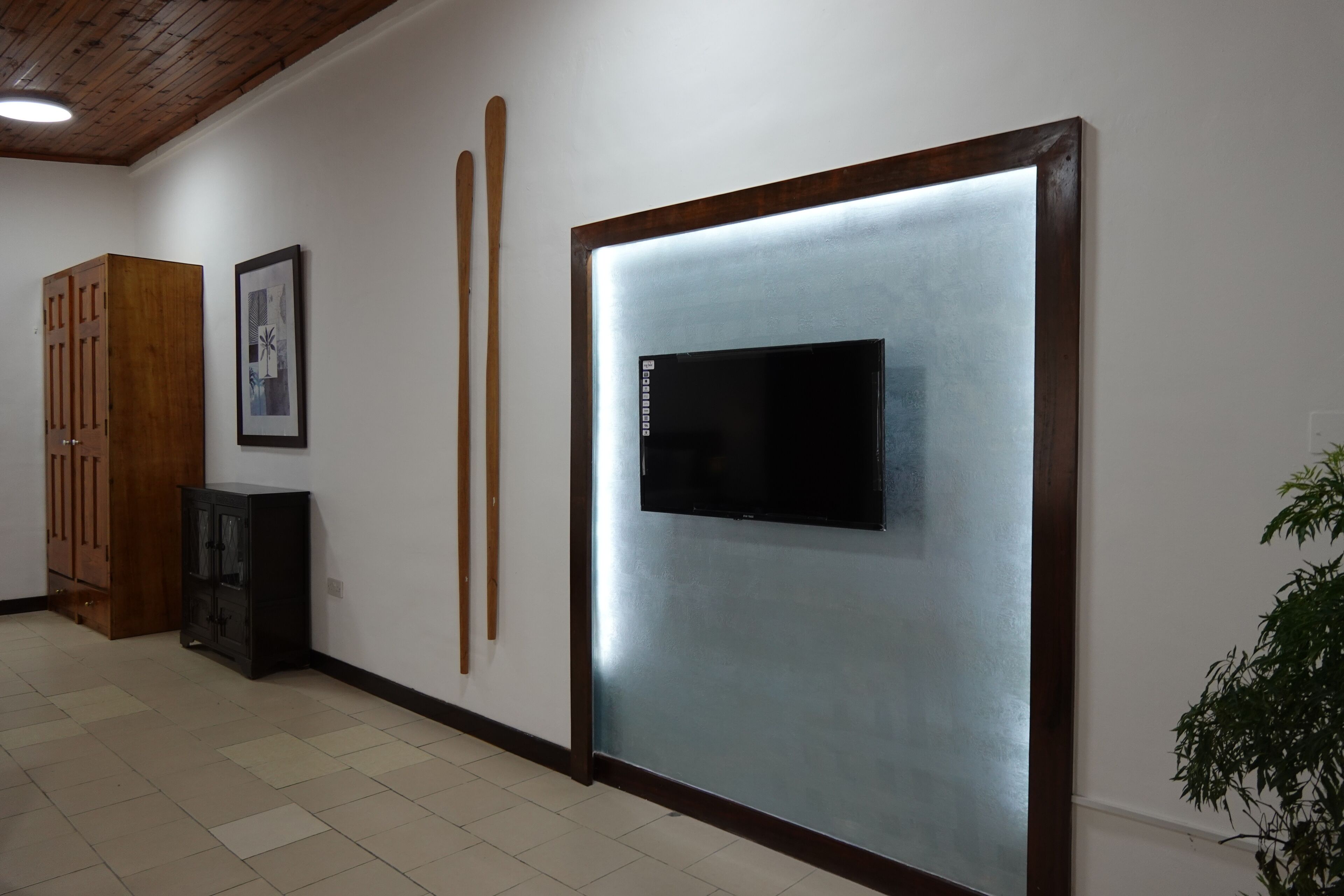 Un pasillo con un armario de madera, un cuadro enmarcado y un televisor montado en la pared.