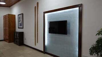 Un pasillo con un armario de madera, un cuadro enmarcado y un televisor montado en la pared.
