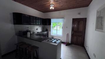 Una cocina con estufa a gas, armarios oscuros, un ventanal y una puerta.
