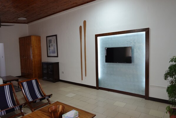 Una sala de estar con televisor montado en la pared, muebles de madera y una planta en maceta.