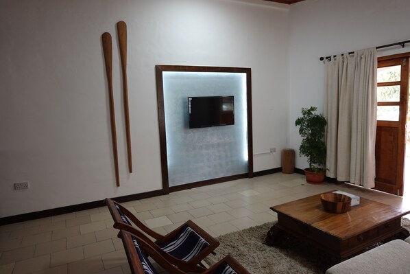A living room with a flat-screen TV mounted on a wall, wooden furniture, a potted plant, and a sliding glass door. - castaway lodge (Pointe Au Sel)