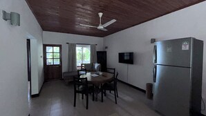 A compact kitchen with a dining table, chairs, a ceiling fan, a refrigerator, and a window with curtains. - castaway lodge (Pointe Au Sel)
