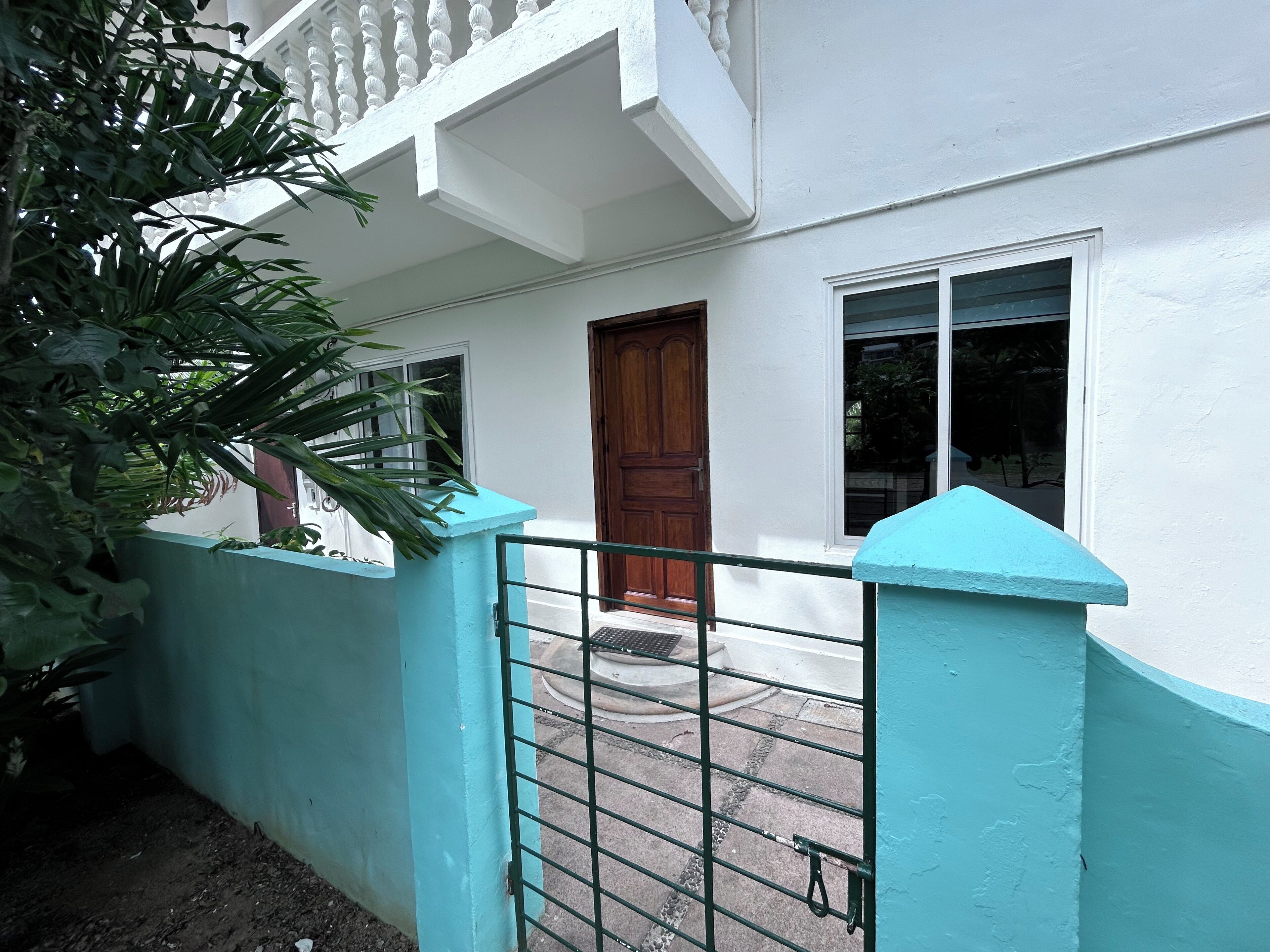 A white building with a blue door and windows, a gated entrance, and a balcony with a white railing.