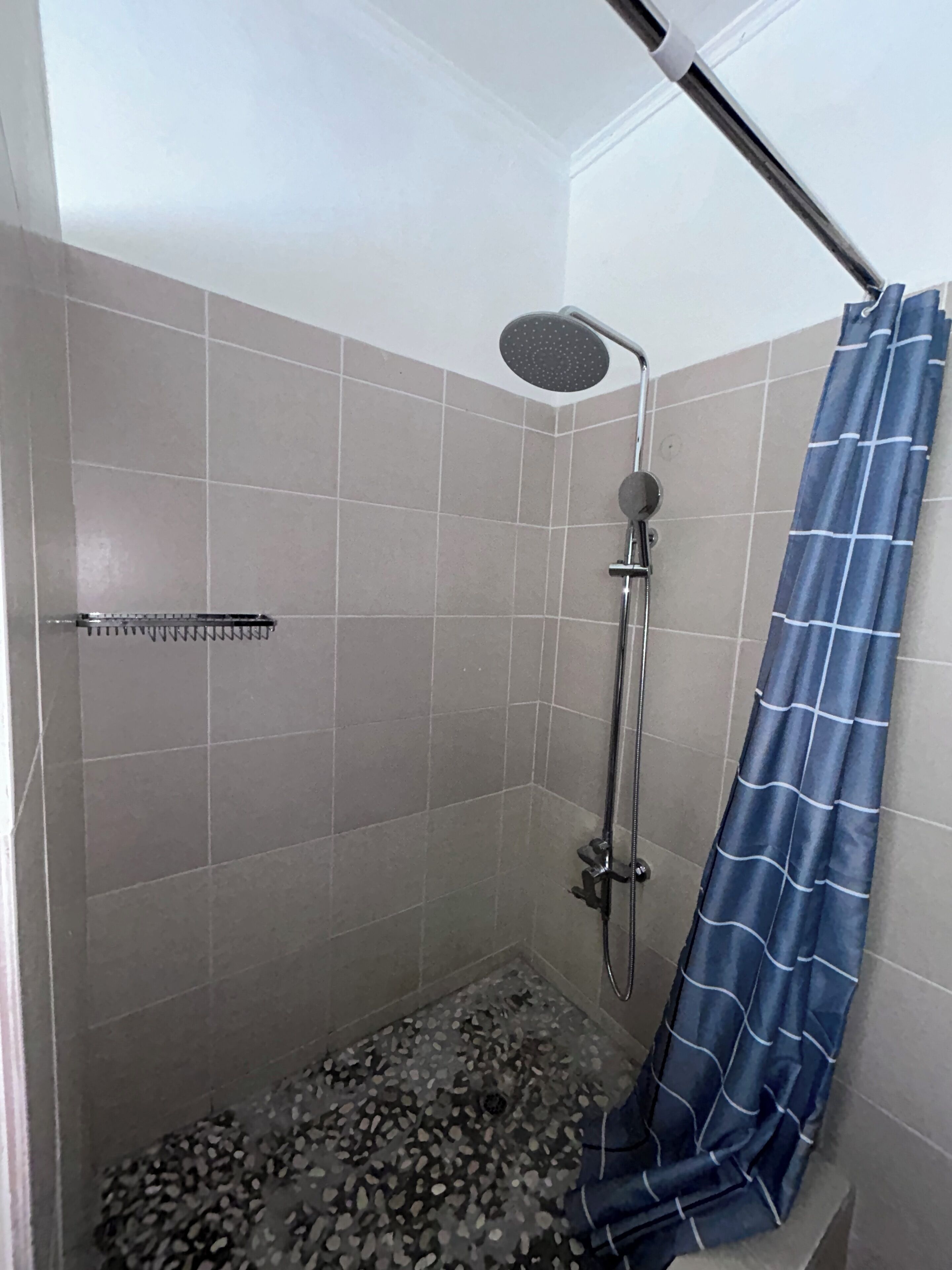 Una ducha con cabezal de ducha de lluvia, cortina de baño azul y suelo de guijarros.
