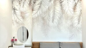 A bedroom with a bed, a desk with a chair, a round mirror, and a wall with a leaf pattern. - Vinhomes Green Bay Apartments (Hanoi)