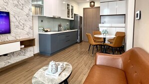 A modern kitchen with a marble backsplash, built-in cabinets, and a dining area with a round table and chairs. - Vinhomes Green Bay Apartments (Hanoi)