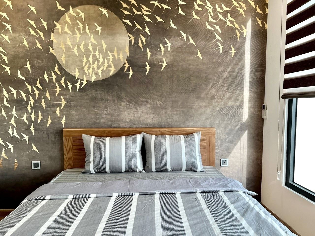 A bedroom with a large bed, striped bedding, a wooden headboard, and a wall with a bird decal.