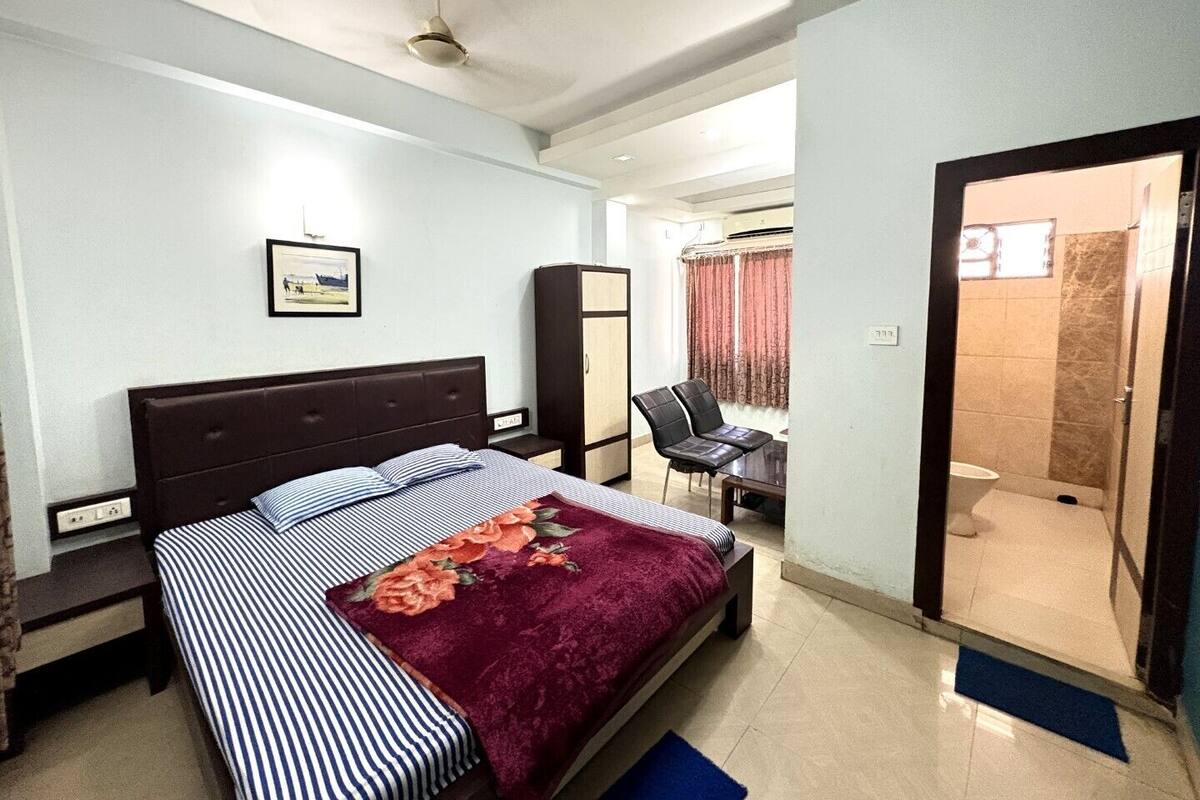 Ein Schlafzimmer mit Bett, Kleiderschrank, Schreibtisch, Stuhl und einem durchgegangene Tür erkennbaren Badezimmer.