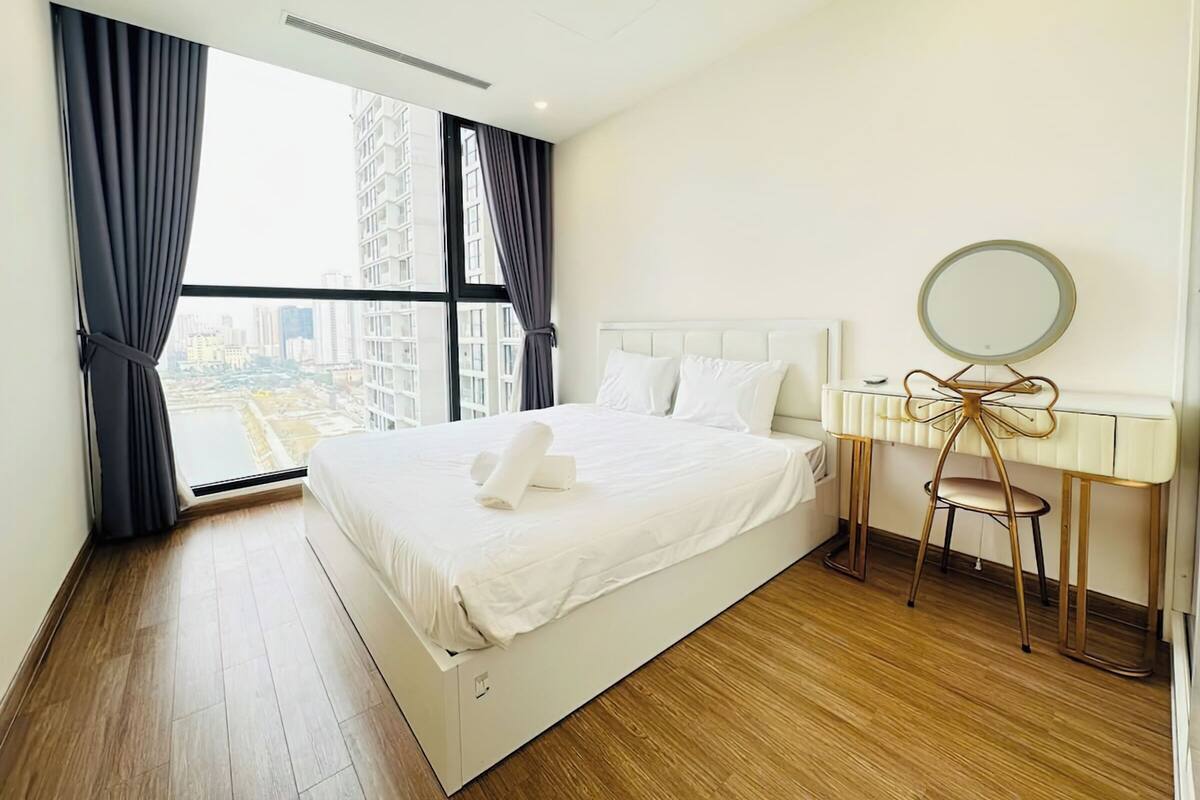 A modern hotel room with a large bed, a vanity with a mirror, and a view of the city through the window.
