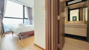 A hotel room with a bed, a large window with curtains, a bathroom with a sink and mirror, and a view of the city. - Vinhomes Skylake by Emily in Town (Hanoi)