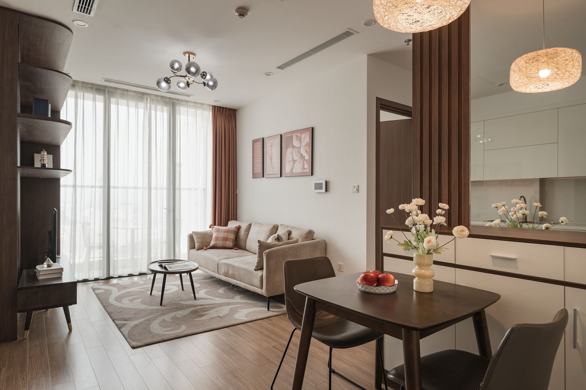 Sala de estar moderna com sofá, mesa de centro e mesa de jantar. Há uma área de cozinha com armários e uma janela florida.