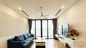 A modern living room with a dark blue sofa, a flat-screen TV, and a decorative vase. - Vinhomes Skylake by Emily in Town (Hanoi)