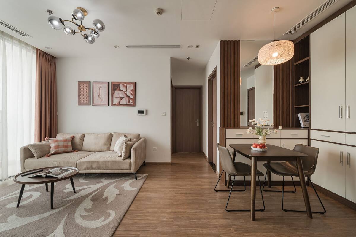 A modern living room with a sofa, coffee table, and dining area with chairs and a table. There is a chandelier and a pendant light.