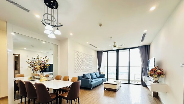 A modern living room with a dining area, a blue sofa, and a large window with curtains. - Vinhomes Skylake by Emily in Town (Hanoi)