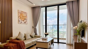 A modern living room with a sofa, a coffee table, and a view of the city through large windows. - Vinhomes Skylake by Emily in Town (Hanoi)