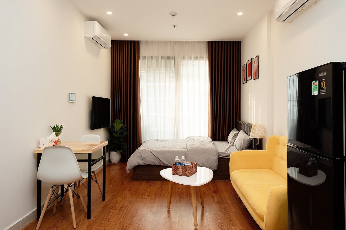 A hotel room with a bed, a sofa, a TV, a desk with a chair, and a small table.