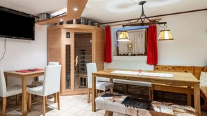 A dining area with a wooden table and chairs, a bench, a television mounted on the wall, and a window with red curtains. - 3-garden apartment Lofer (Reit im Winkl)