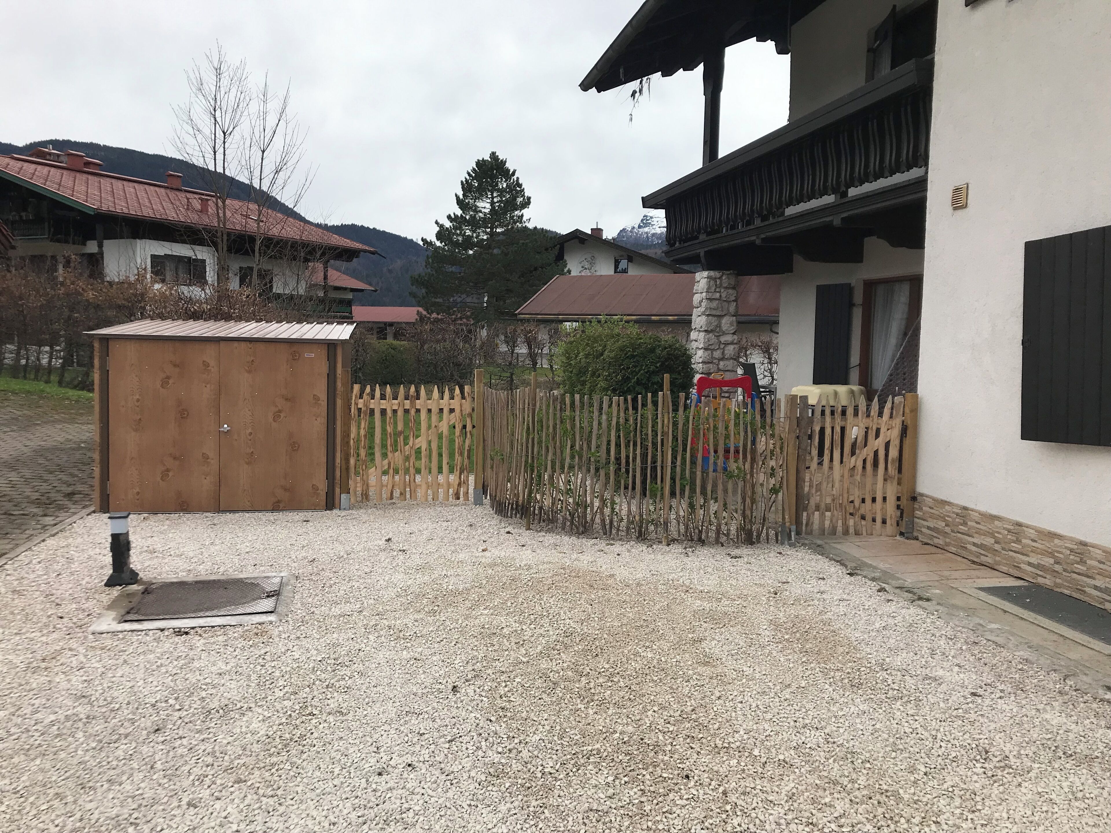 Un barrio residencial con camino de grava, valla de madera y un cobertizo pequeño.