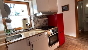 A compact kitchen with white cabinets, a red refrigerator, a tiled backsplash, and a wooden floor. - 3-garden apartment Lofer (Reit im Winkl)