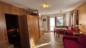 A cozy room with a wooden wardrobe, a red sofa, a dining table, and a ceiling light. - 3-garden apartment Lofer (Reit im Winkl)
