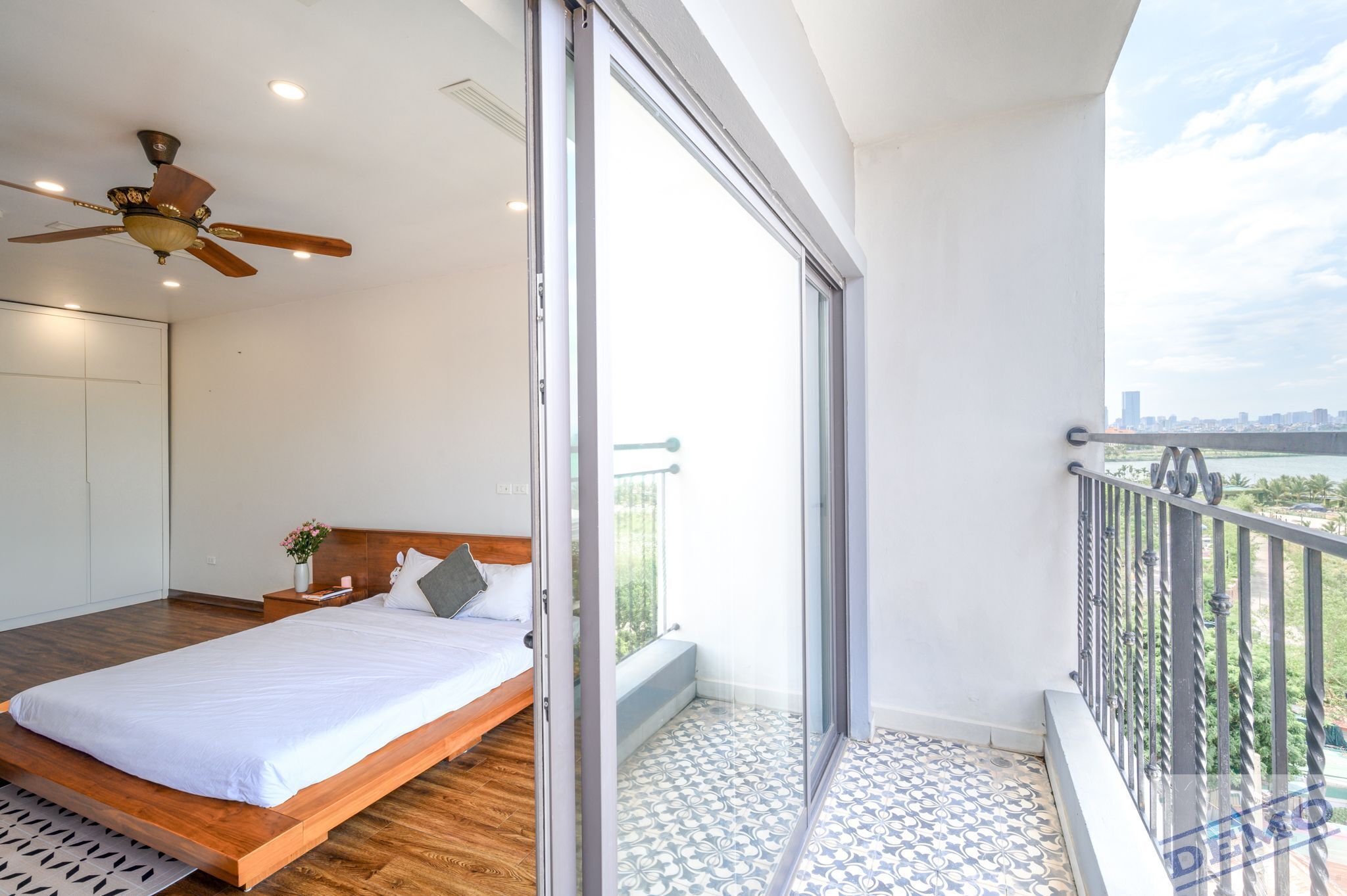 A bedroom with a wooden bed, a ceiling fan, and a balcony with patterned flooring.