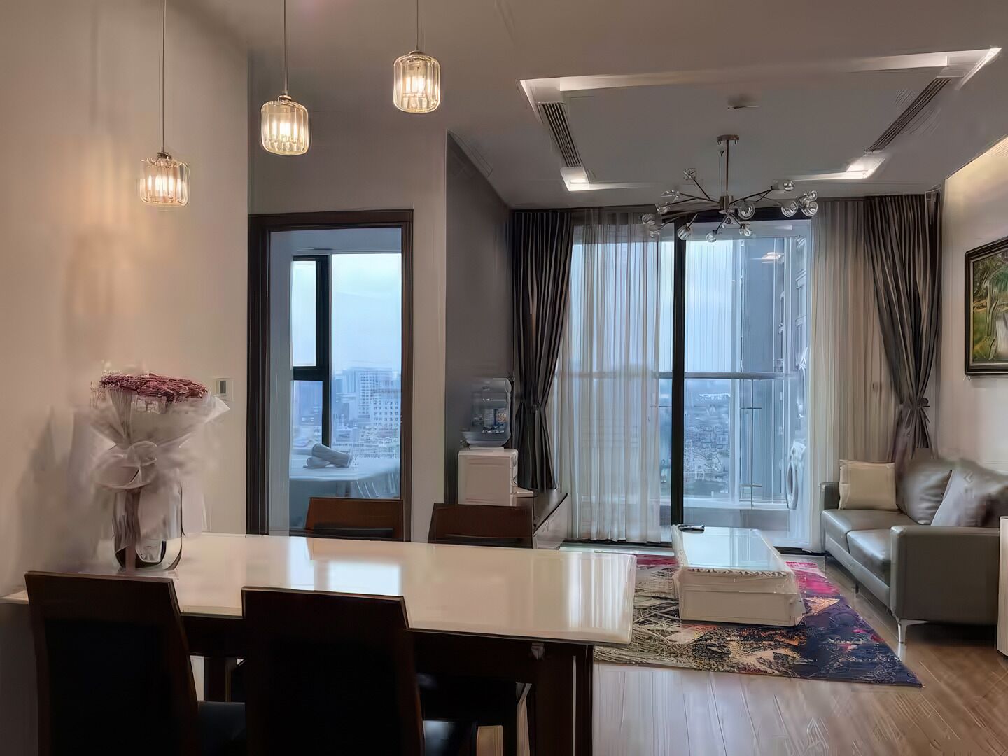 A modern living room with a dining area, large windows, and a city view.