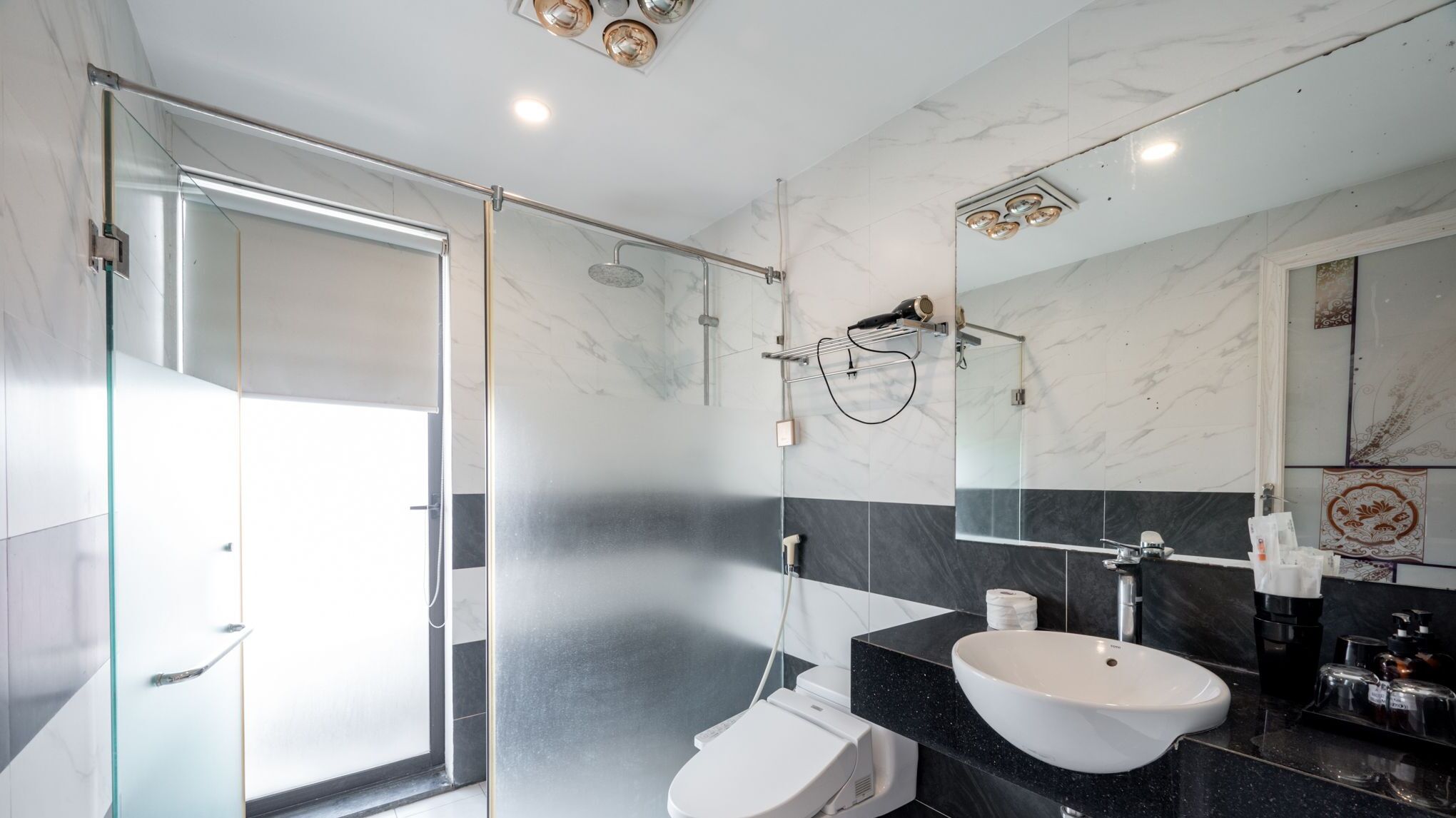 A modern bathroom with a glass shower enclosure, a white toilet, a black marble sink, and a large mirror.