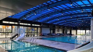 Ein Hallenbad mit Glasdach, Rutschen und Liegestühlen.