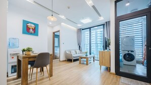 Ein modernes Wohnzimmer mit einer Couch, einem Couchtisch und einem Essbereich. Ein Wasserspender und eine Waschmaschine sind sichtbar.