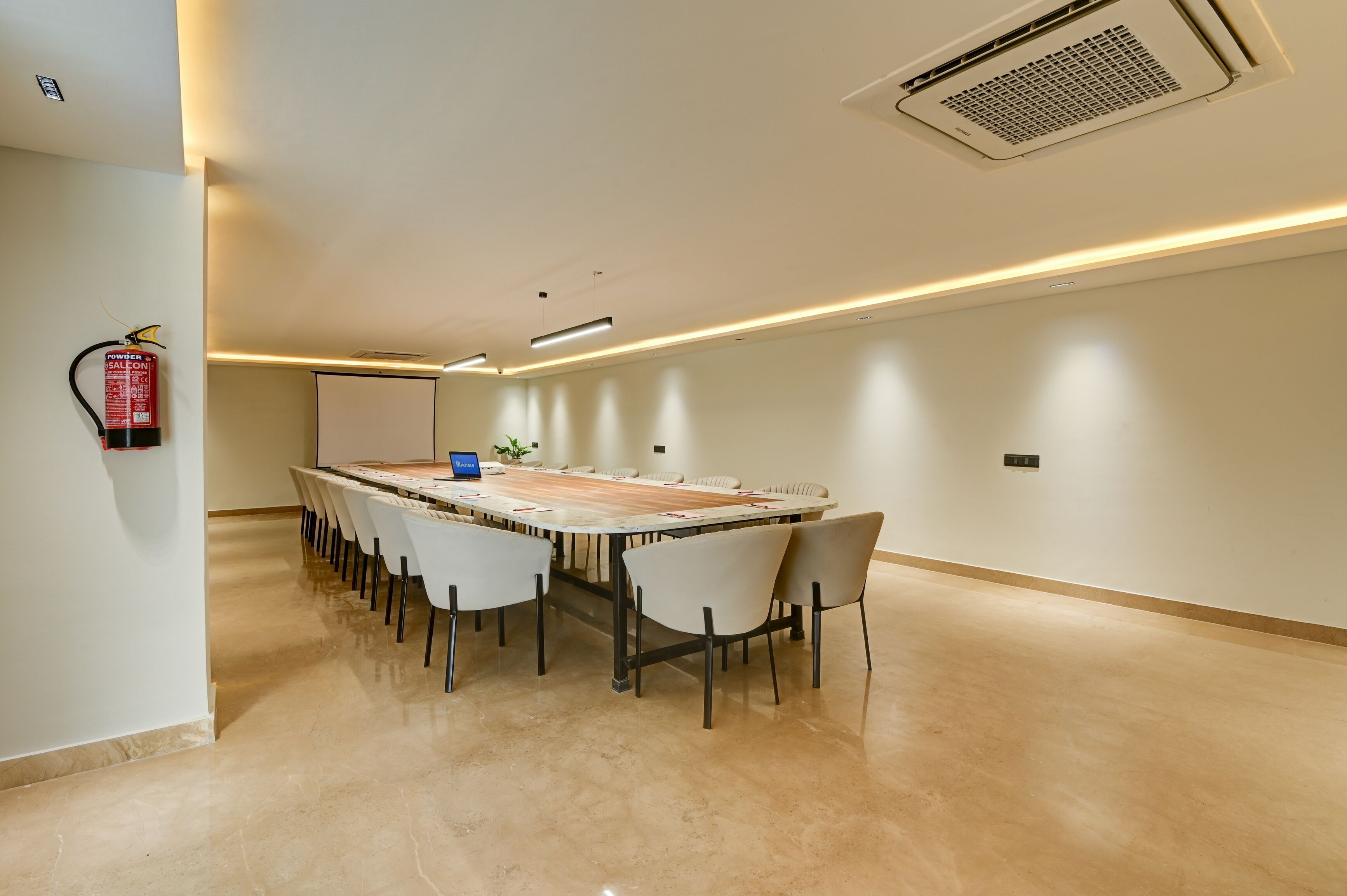A conference room with a long table, chairs, a fire extinguisher, and a ceiling vent.