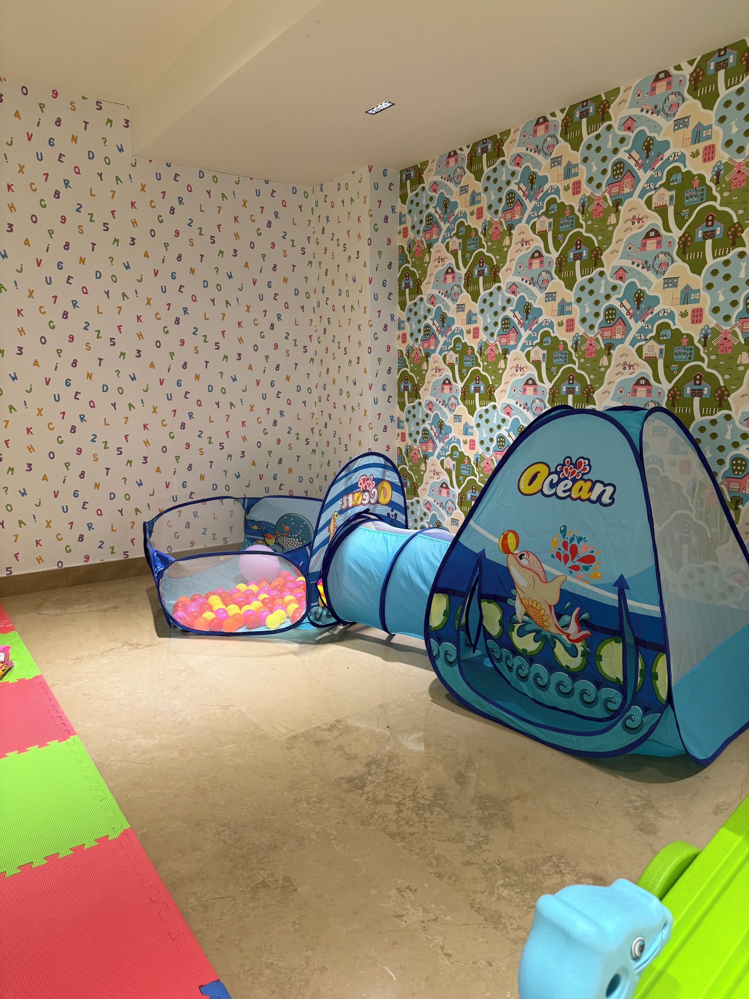 A play area with a tunnel and ball pit, surrounded by colorful walls with alphabet patterns and farm-themed wallpaper.
